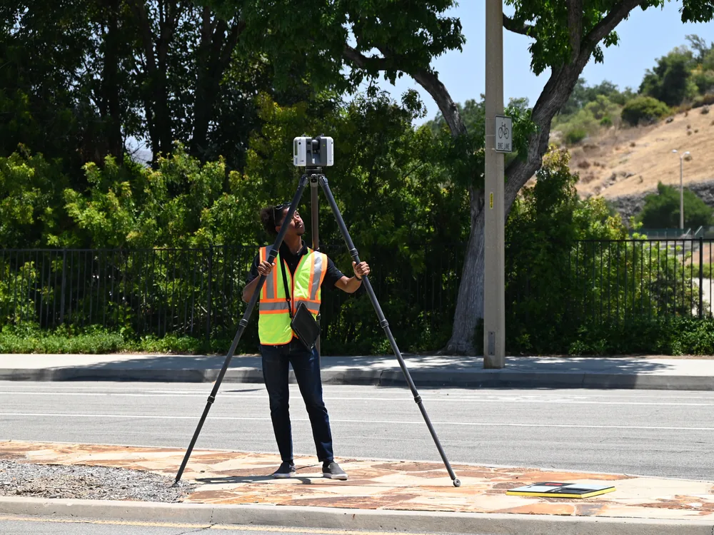 A technician operating a survey instrument at a roadside