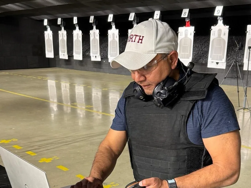 An investigator in a ballistic vest at a laptop on an indoor firing range