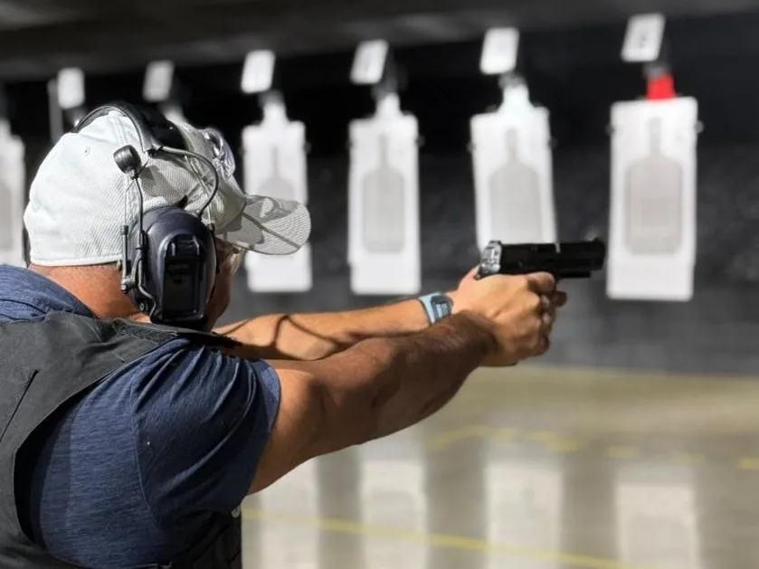 A shooter in hearing protection firing a pistol at paper targets down a range